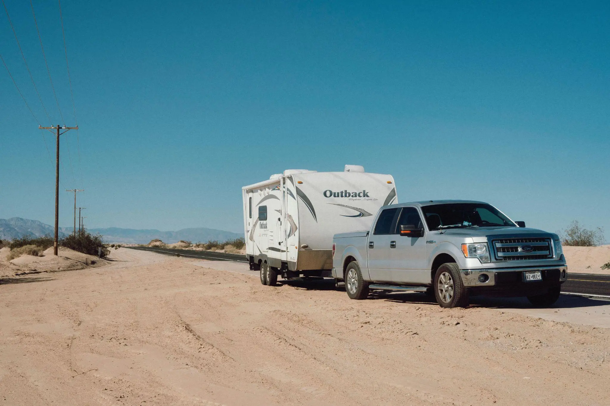 Silver Ford F‑150 towing Outback trailer on desert highway 